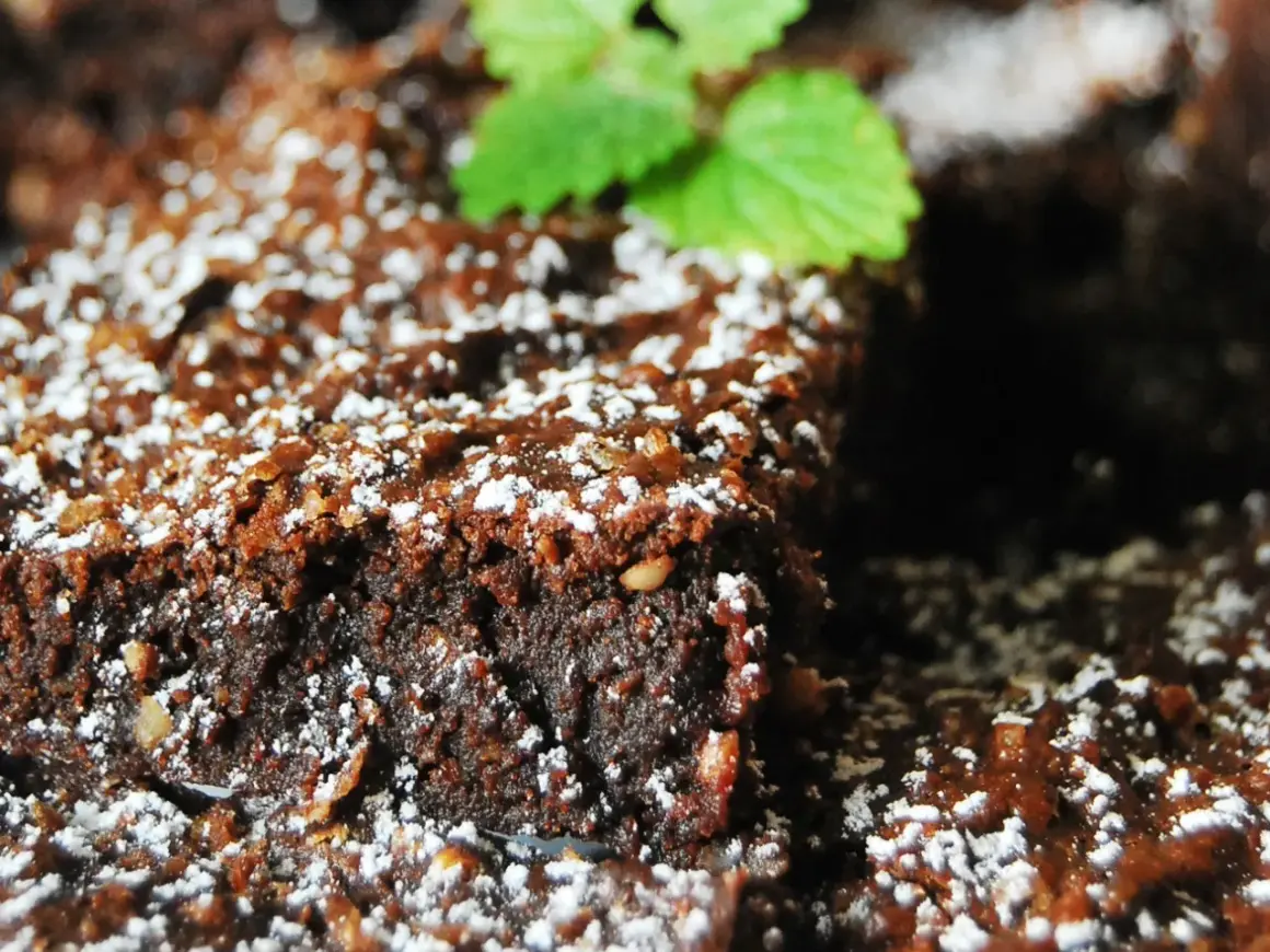 Wilgotny brownie z malinami, posypany cukrem pudrem i udekorowany listkiem mięty. Idealny deser na każdą okazję.
