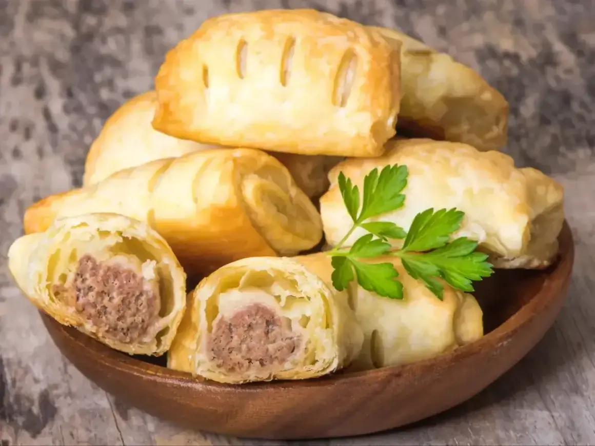 Stos pieczonego ciasta francuskiego z kiełbasą w środku, ozdobione natką pietruszki.