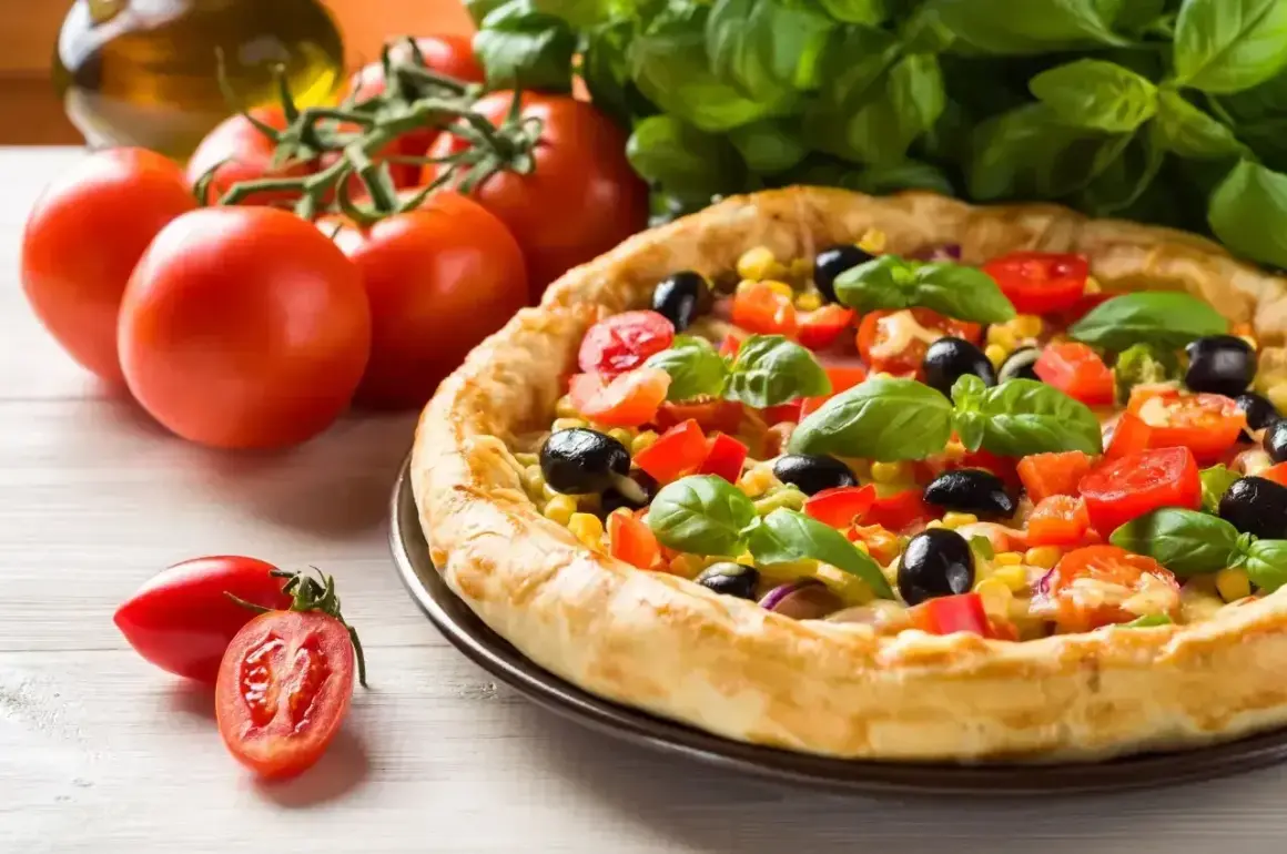 Pyszna pizza z pomidorami, oliwkami i kukurydzą, obok świeże pomidory i bazylia. Idealna na letni obiad.