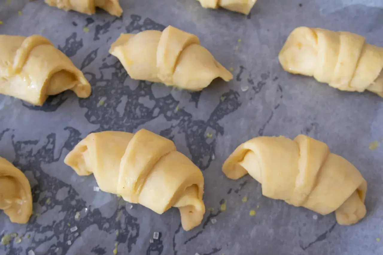 Gotowe do pieczenia rogaliki krucho drożdżowe, ułożone na papierze do pieczenia, posypane cukrem.