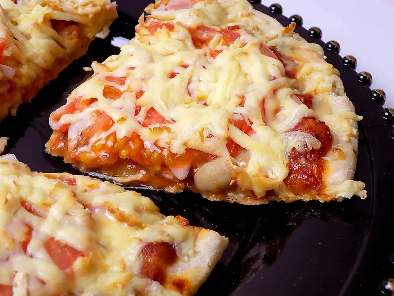 Pyszna pizza z patelni, z ciągnącym się serem, pomidorami i kawałkami kiełbaski, podana na czarnym talerzu.