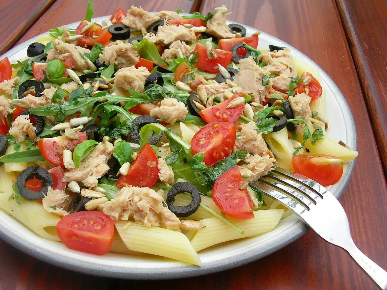 Pyszna sałatka z makaronem penne, tuńczykiem, pomidorkami, oliwkami i rukolą, posypana słonecznikiem.