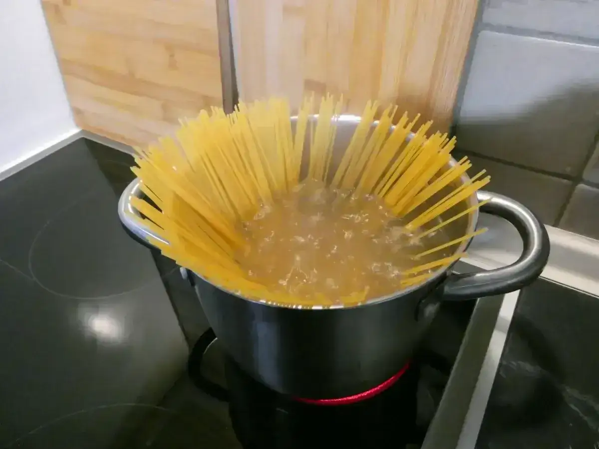 Gotujesz makaron spaghetti w garnku na kuchence. To pierwszy krok, jak zrobić spaghetti.