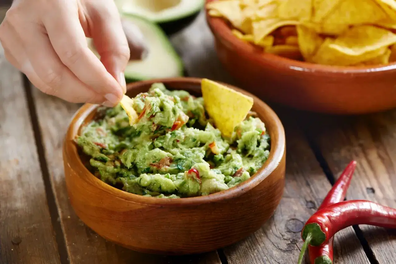Ręka zanurza chipsa w misce z guacamole. To pyszne, zielone danie, które warto znać!