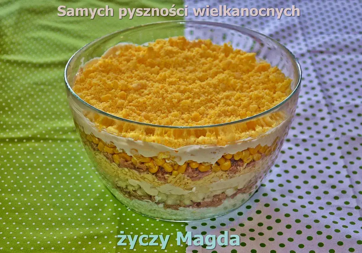 Warstwowa sałatka z tuńczykiem, kukurydzą i jajkiem, posypana żółtym sypkim serem. Idealna na wielkanocny stół.