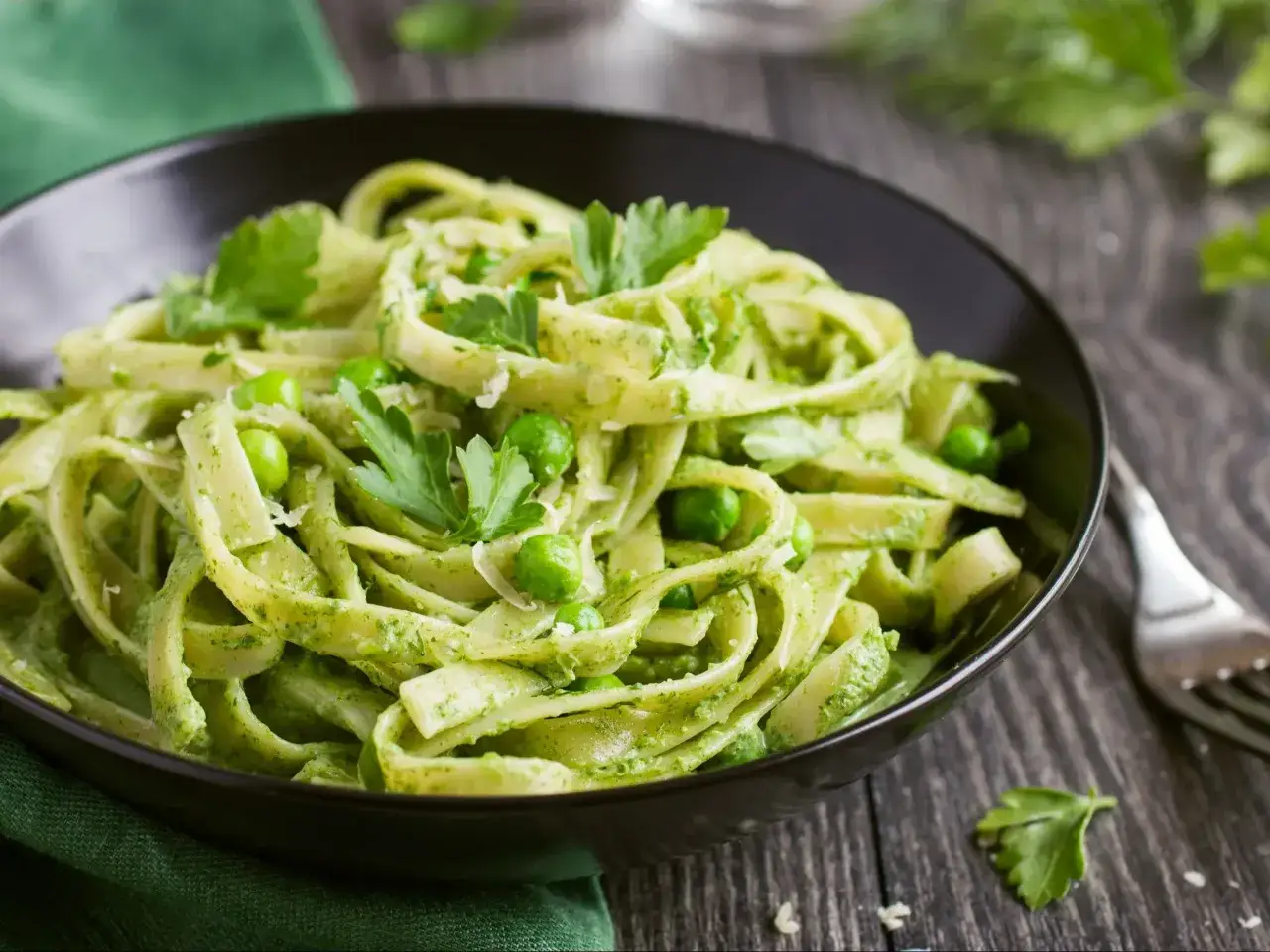 Talerz pełen makaronu z pesto, groszku i listków pietruszki. Pyszne danie, które zachwyca świeżością i kolorem.