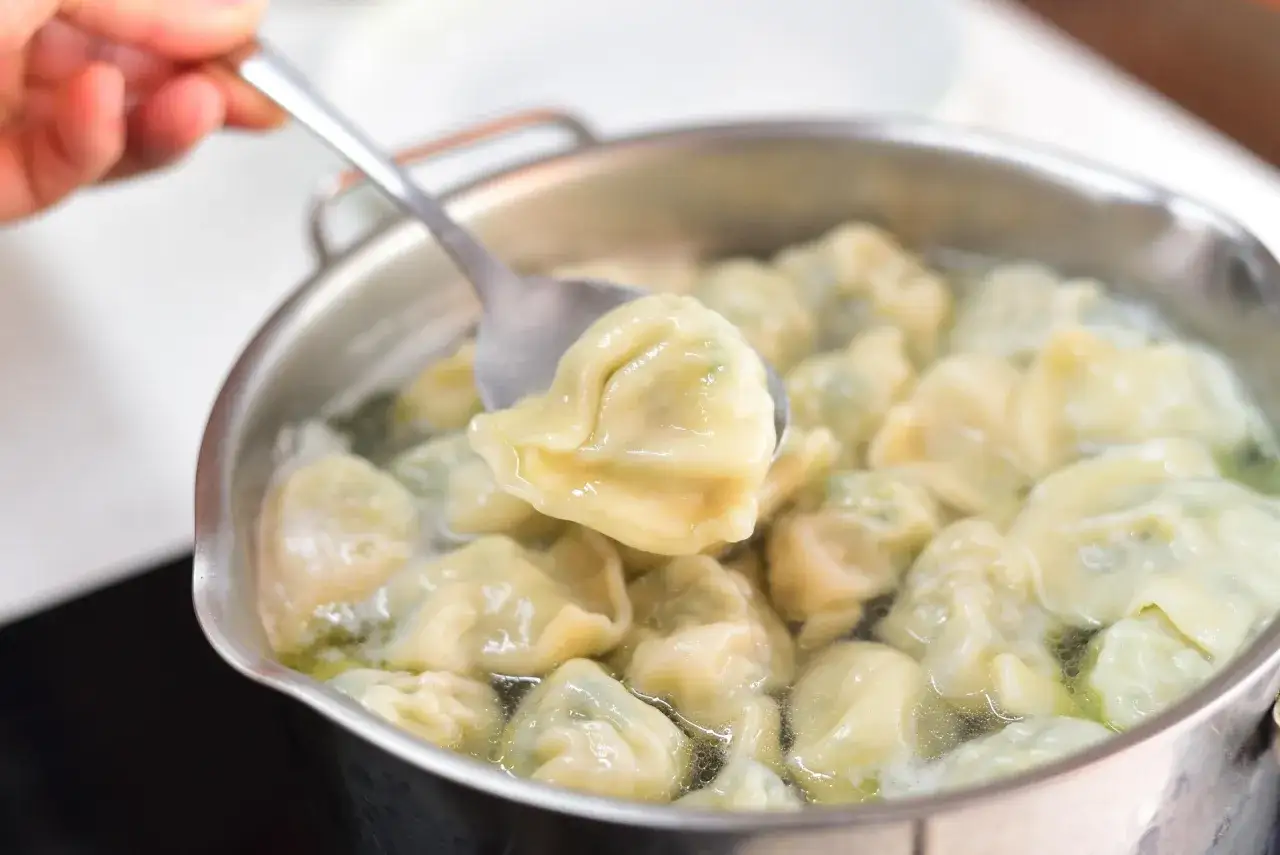 Gotowanie pierog&oacute;w: łyżka wyciąga jednego z garnka, by sprawdzić, ile gotować.