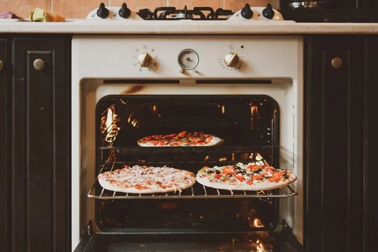 Trzy pyszne pizze pieką się w piekarniku. Jedna na górnej półce, dwie na dolnej.