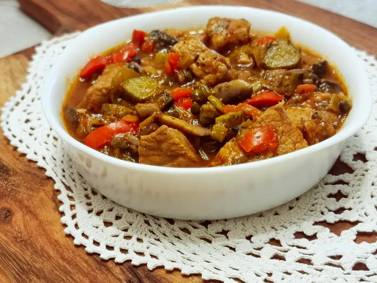 Aromaticzny strogonow z wieprzowiny i pieczarek, pełen kawałk&oacute;w mięsa, papryki i og&oacute;rka, podany w białej misce na koronkowym serwecie.