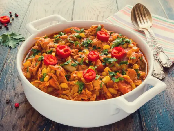 Aromaticzny gulasz z kurczaka z kukurydzą i papryczką chili, posypany świeżą natką pietruszki, podany w białej misie.
