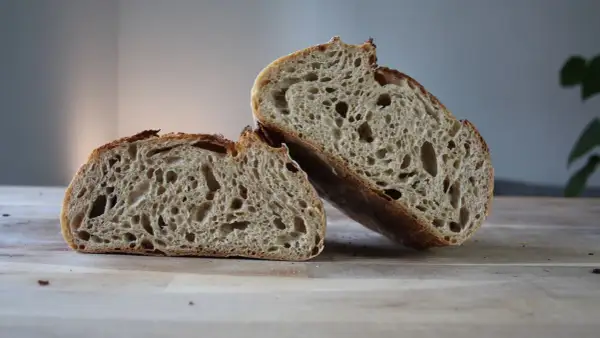 Chleb pszenno żytni na zakwasie, przekrojony na pół, ukazuje puszysty miąższ z licznymi dziurami i chrupiącą skórkę.