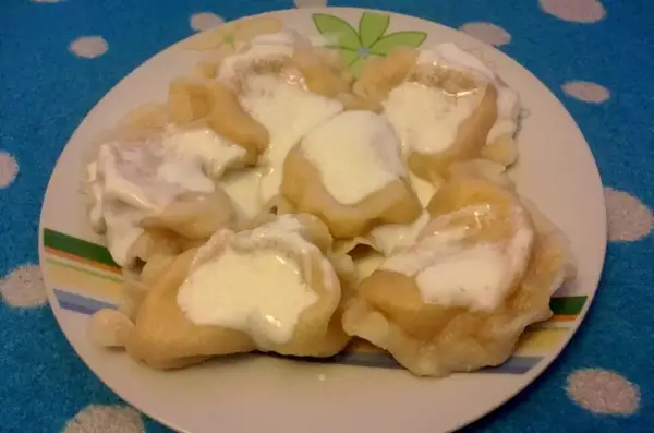 Talerz pełen pysznych pierogów ruskich, polanych śmietaną. Idealne na obiad, zgodnie z tradycyjnym pierogi ruskie przepis.