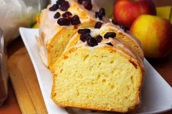 Szybka babka wilgotna, polana lukrem i posypana żurawiną, obok jabłek. Idealna na deser.