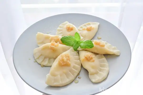 Pyszne pierogi z serem, udekorowane miętą i posypką, ułożone na talerzu w kształt kwiatu.