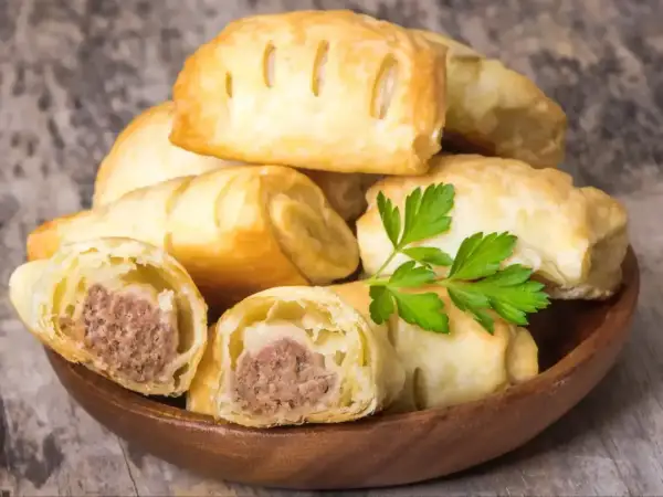 Stos pieczonego ciasta francuskiego z kiełbasą w środku, ozdobione natką pietruszki.